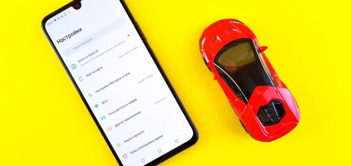 A smartphone and toy car placed on a bright yellow background viewed from above.